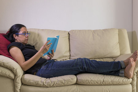 A caucasian girl enjoying a book on a sofaの写真素材