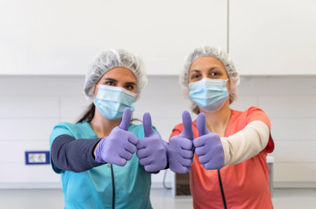 Two young medical workers looking at camera, holding thumbs up, positive, happy, hospital, mask,...