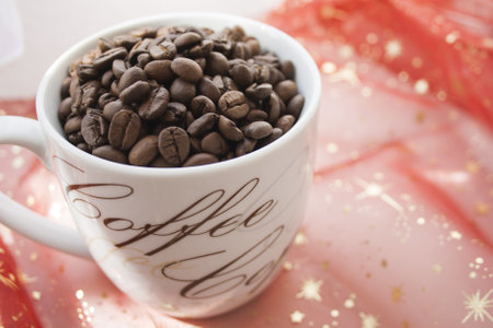 A closeup of a mug filled with roasted coffee beans on the red fabricの写真素材