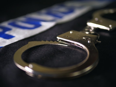 Handcuffs and police tape on black background close up shot