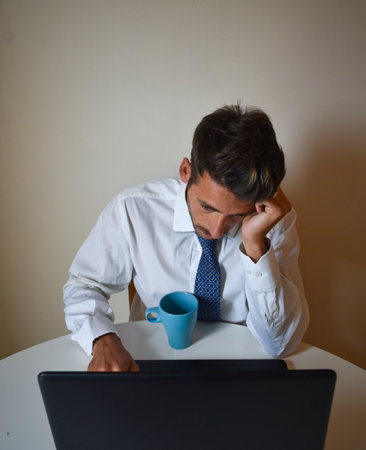 A tired businessman leaning his head on his hand while working on his laptopの写真素材
