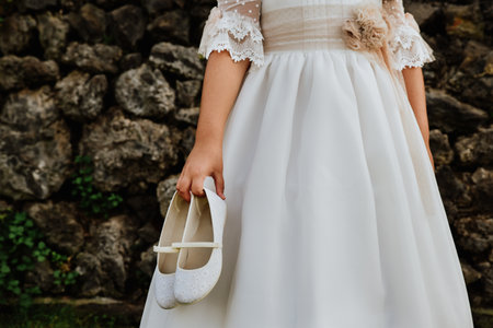 A communion girl with white dress holding white shoesの写真素材