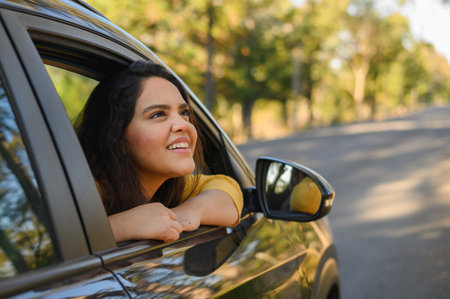 A young Hispanic woman enjoying sun out of car window on a bright day - road trip concept