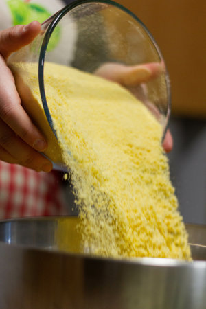 A closeup of a baker pouring yellow flour into a bowl of pastry ingredientsの写真素材
