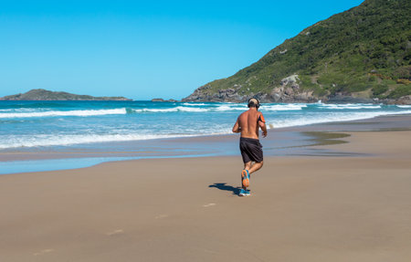 A male walking listening to music with headphones on a sandy beach in Brazilの写真素材