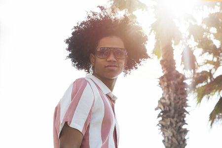 A portrait of a cool looking young African man with a palm tree and sunlight in the backgroundの写真素材