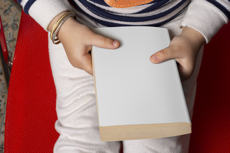 A little girl holding a novel book with blank cover, editable mockup template ready for design - cover selection path includedの写真素材