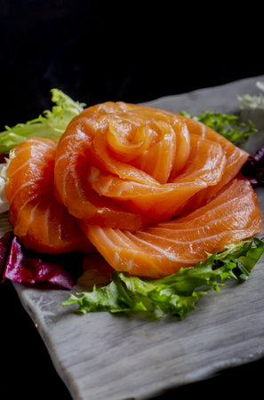 A vertical shot of salmon sashimi decorated in flower on a dark backgroundの写真素材
