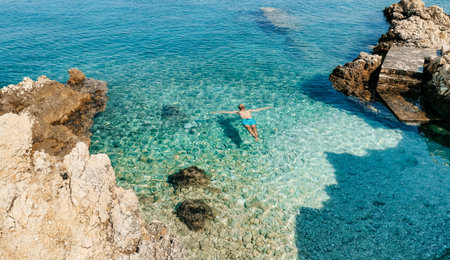 Young tourist relaxing and floating on water surface on beautiful hidden beach with transparent water on Pag island in Croatia.の写真素材