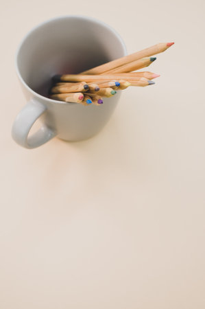 A top view closeup of colored pencils put in a white mug on a brown backgroundの写真素材