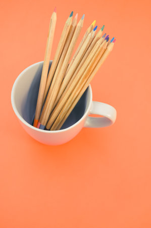 A top view closeup of colored pencils put in a white mug on an orange backgroundの写真素材