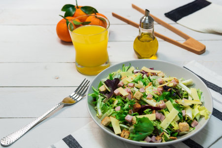 A plate of fresh Mediterranean salad with olive oil served with orange juice on a white wooden tableの写真素材