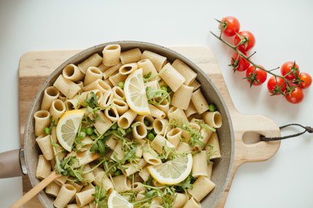 A shot of a pan of rigatoni pasta with lemons, greens, and cherry tomato decoration ready for serving.の写真素材