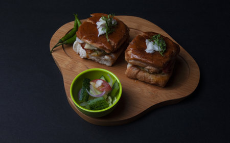 A closeup shot of biscuit sandwiches and side salad on a wooden tray on a black backgroundの写真素材