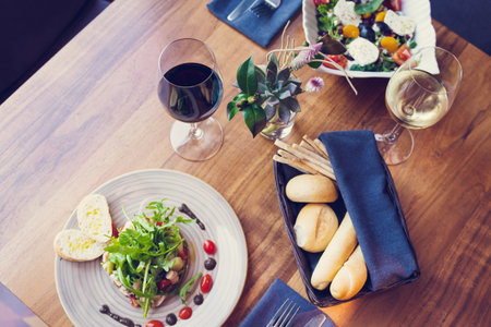 A top view of a dinner table with a plate of salad, a glass of wine and a plate of breadの写真素材