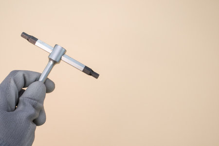 A closeup shot of a hand wearing gloves holding a socket wrench isolated on pink backgroundの写真素材