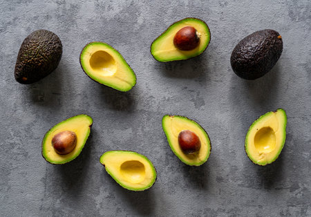A creative top view of sliced and whole avocados on a grey background