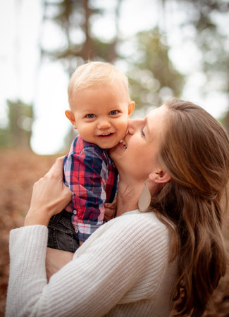 An adorable little boy smiling at the camera while his mother is hugging and kissing him