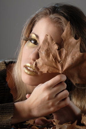 An Argentinian Blonde woman with bright gold makeup and dried leaves in fall styeの写真素材
