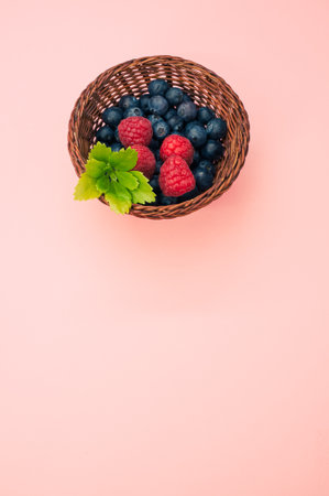 A top view of blueberries raspberries and leaves in a basket