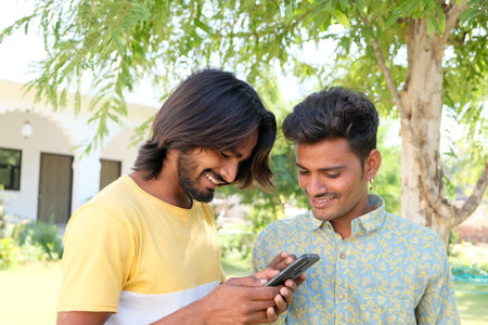 A portrait of two happy Indian males in the park using a smartphoneの写真素材