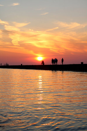 A vertical shot of silhouettes of people on a pier at Station Beach with sunlight reflected in waterの写真素材