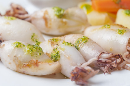 A closeup of boiled squids with green sauce, boiled potatoes, and carrots on a plaの写真素材