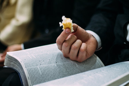 A closeup shot of a person holding the holy bread with a bible on his lap