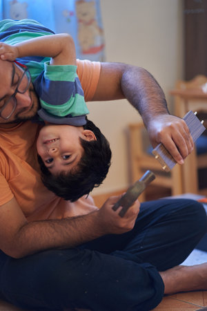 Son has fun on top of his father while assembling furniture. Assembling furniture at home. Carpentry sessionの写真素材