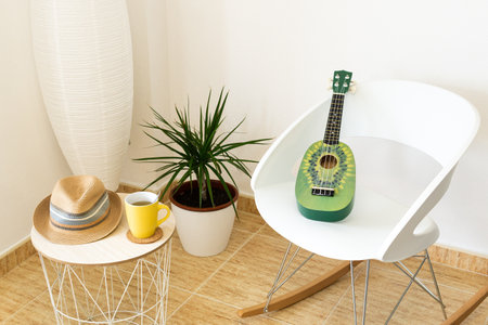 A green ukulele on a chair in a studio with a table and potted plantの写真素材