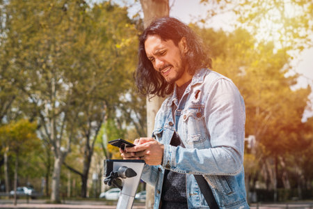 Man with long hair using his phone with a beautiful backlight at the parkの写真素材