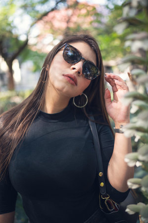 A cool sexy Mexican woman in sunglasses posing with a hand up in a garden