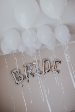 A vertical shot of white balloons with helium and silver balloons with "BRIDE" letters on the wallの写真素材