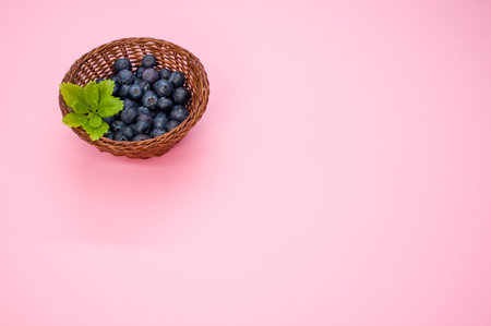 A top view of blueberries and a leaf in a basket on a pink backgroundの写真素材
