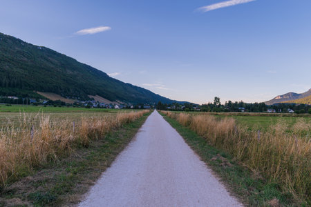 A beautiful view of a narrow road in a grassy field surrounded by rocky mountainsの写真素材