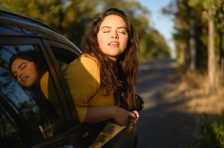 A young Hispanic woman enjoying sun out of car window on a bright day - road trip conceptの写真素材