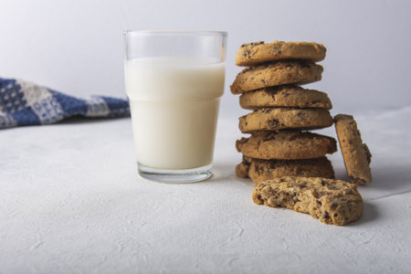 A stack of peanut butter cookies by a glass of fresh milk on a white tableの写真素材