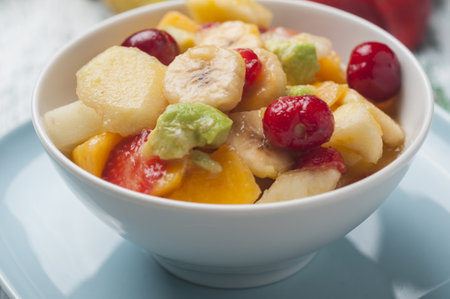 A closeup shot of a bowl full of fresh sliced strawberries, melon, apple cherry, banana, and avocadoの写真素材