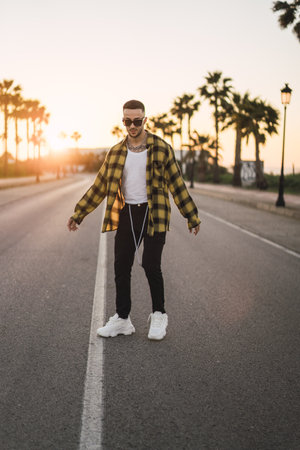A vertical shot of a stylish European man standing on a road at sunsetの写真素材