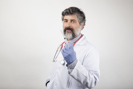 A Caucasian doctor in a white uniform with a syringe and gloves on white backgroundの写真素材