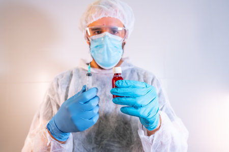 A male doctor in a protective suit preparing a syringe for vaccinationの写真素材