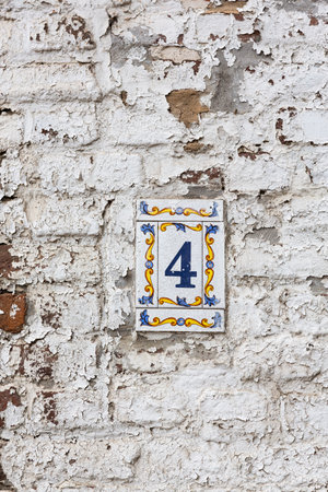 A vertical shot of the number 4 on a square board with decorations on an old brick wallの写真素材