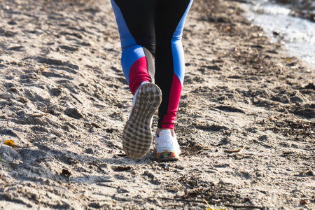 A shallow focus of a woman jogging at a sandy beach