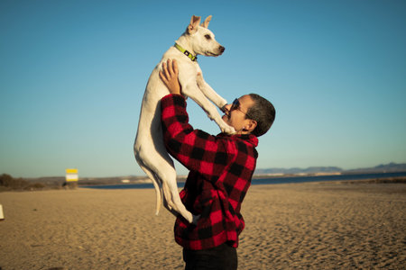A shallow focus shot of a female with sunglasses playing with her white dog on the beachの写真素材