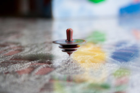 A selective focus shot of a spinning top on a colorful table with light hitting itの写真素材