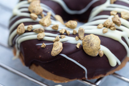 A closeup shot of an appetizing chocolate-covered raw donut with nuts sprinkles on blurry backgroundの写真素材