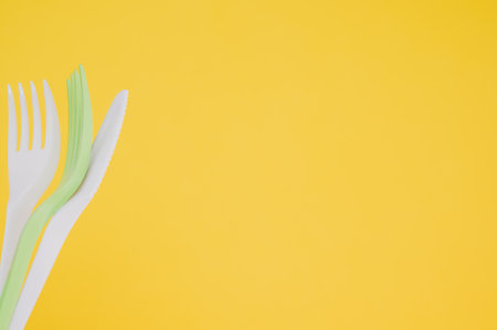A closeup shot of plastic forks and a knife on a yellow backgroundの写真素材