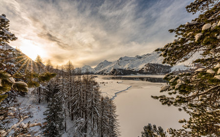 A breathtaking view of the snowy mountains gleaming under the sunrays in Engadin, Switzerlandの写真素材