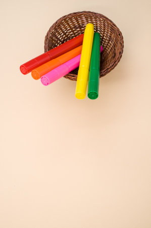 A closeup shot of colorfulmarkers on a small woven basket isolated on a pink backgroundの写真素材