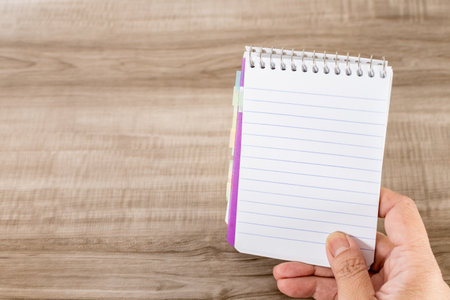 A female hand holding a notebook on a wooden desk
